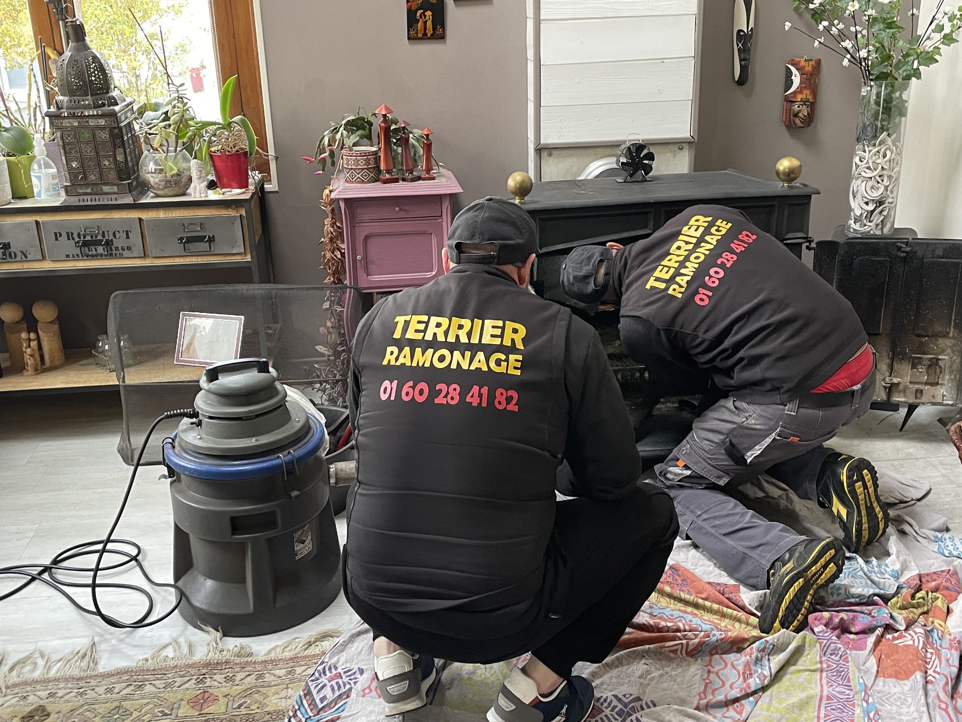 Deux ramoneurs Terrier Ramonage en intervention sur un poêle à bois, sol protégé par des bâches